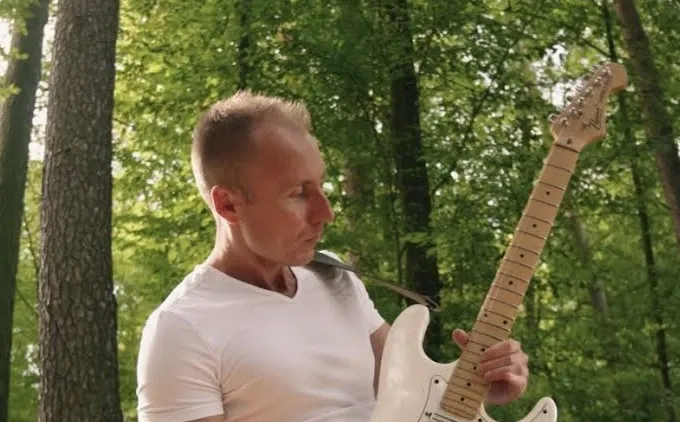 Radosław Roszkiewicz (Vince Rock) z białym Stratocasterem — kadr z teledysku „Faith”